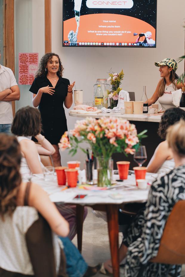 Jacqueline opening the room at Entre Manos, guests seated around a long table